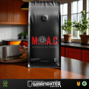 Black coffee bag with 'M.A.C Mother of All Coffee' branding on a kitchen counter.